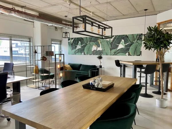 Moderne kantoorruimte aan de Anthony Fokkerweg met houten tafels, groene meubels en een tropisch wandpaneel.